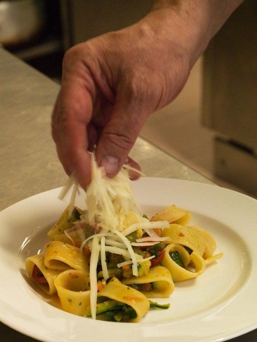 A hand putting cheese shavings on a plate of pappardelle
