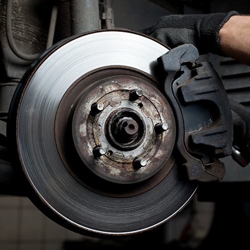Car brake rotor and caliper being inspected by a gloved hand.