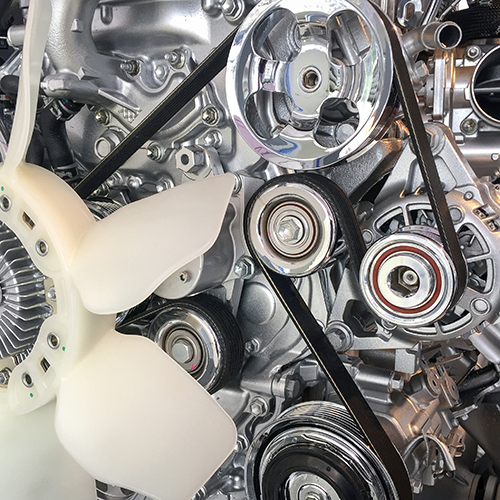 Close-up of a shiny silver engine with black belts, pulleys, and a white fan.