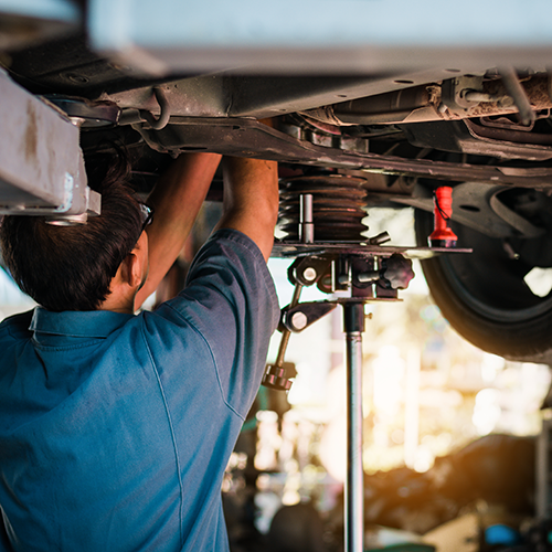 Mechanic working under a car on a lift in a garage.