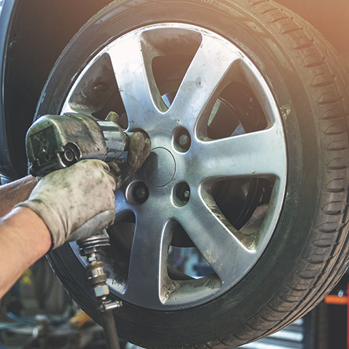 Mechanic using a pneumatic wrench to remove a wheel from a car.