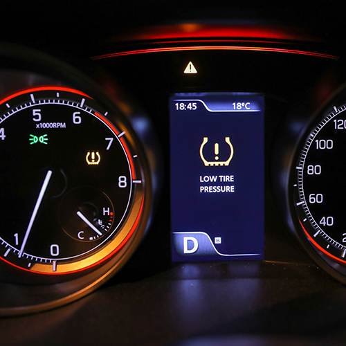 Car dashboard displaying a low tire pressure warning, speedometer, tachometer, and other gauges.