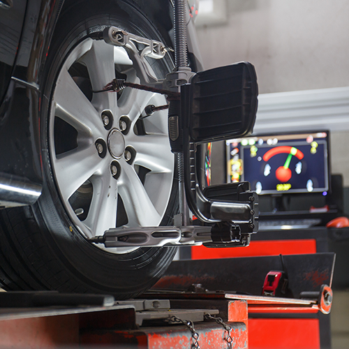 Car wheel undergoing alignment in a repair shop. Black and silver equipment; monitor shows readings.