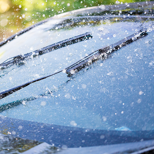 Windshield wipers clearing a rain-covered windshield. Water droplets and blurred green background.