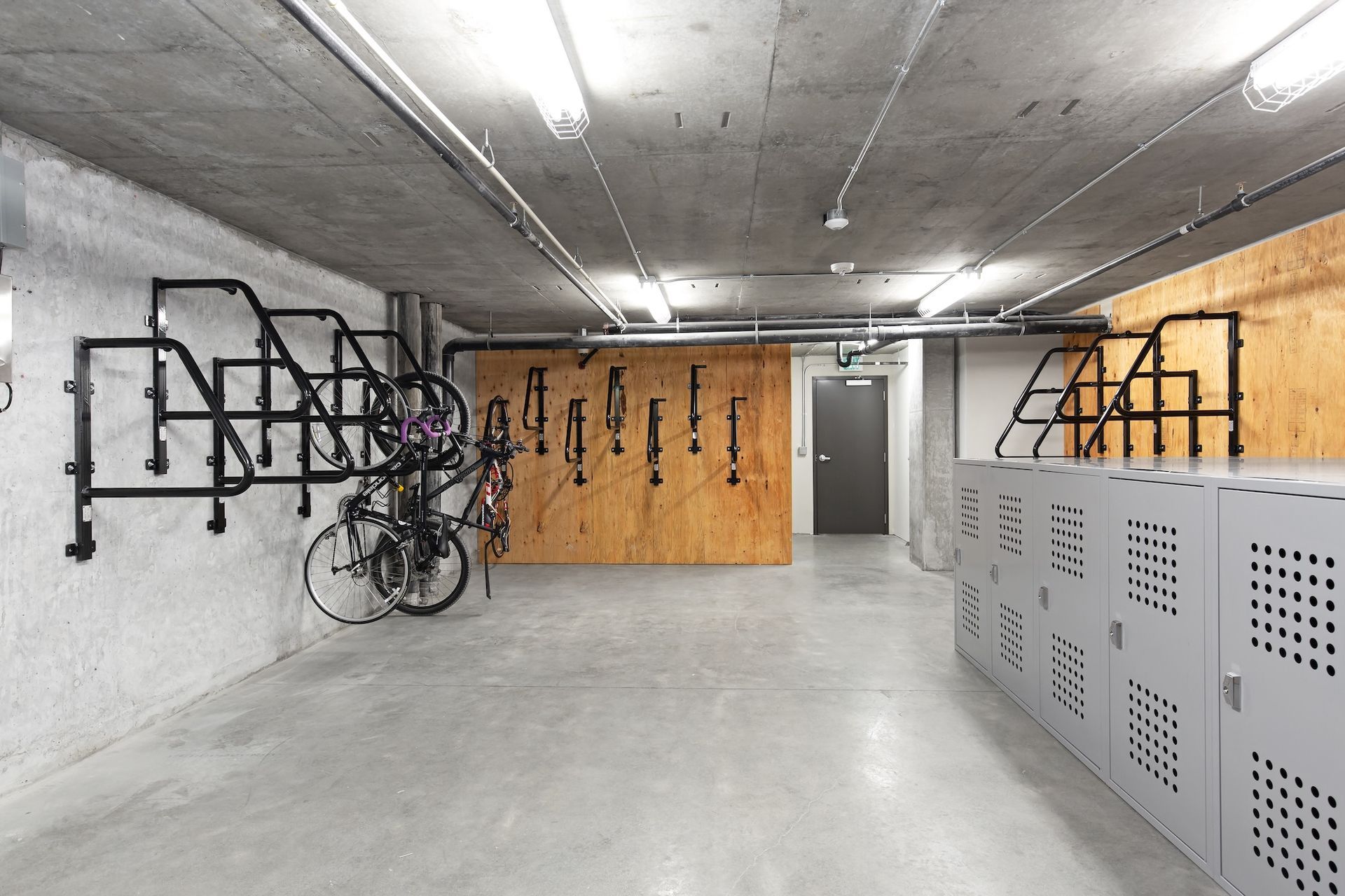 Bike storage room with racks, lockers, and concrete floor.