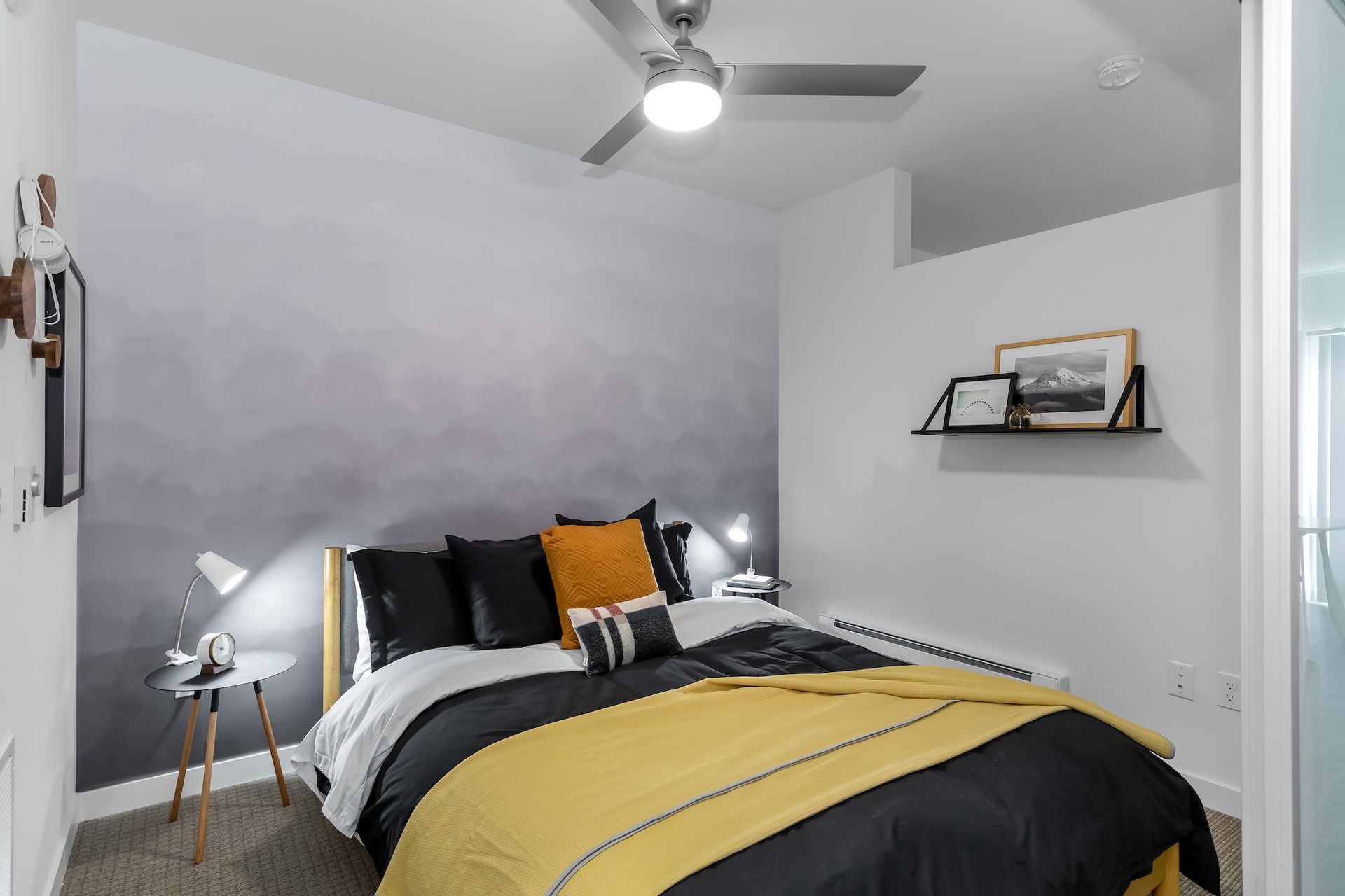 Bedroom with a gray-gradient accent wall, black and yellow bedding, and a small side table with a lamp.