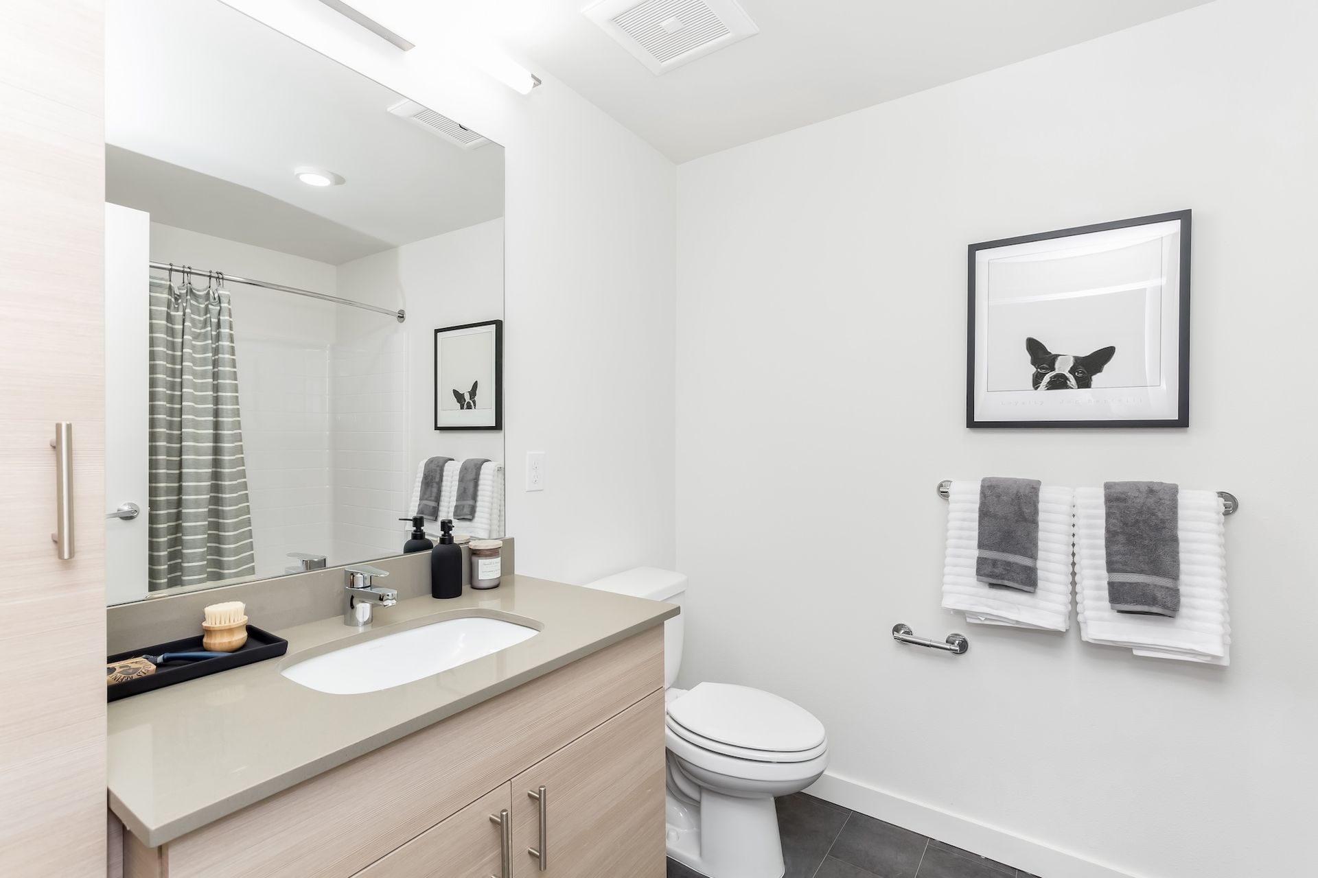 Bathroom with sink, toilet, neutral color scheme, artwork, and gray towels on a bar.