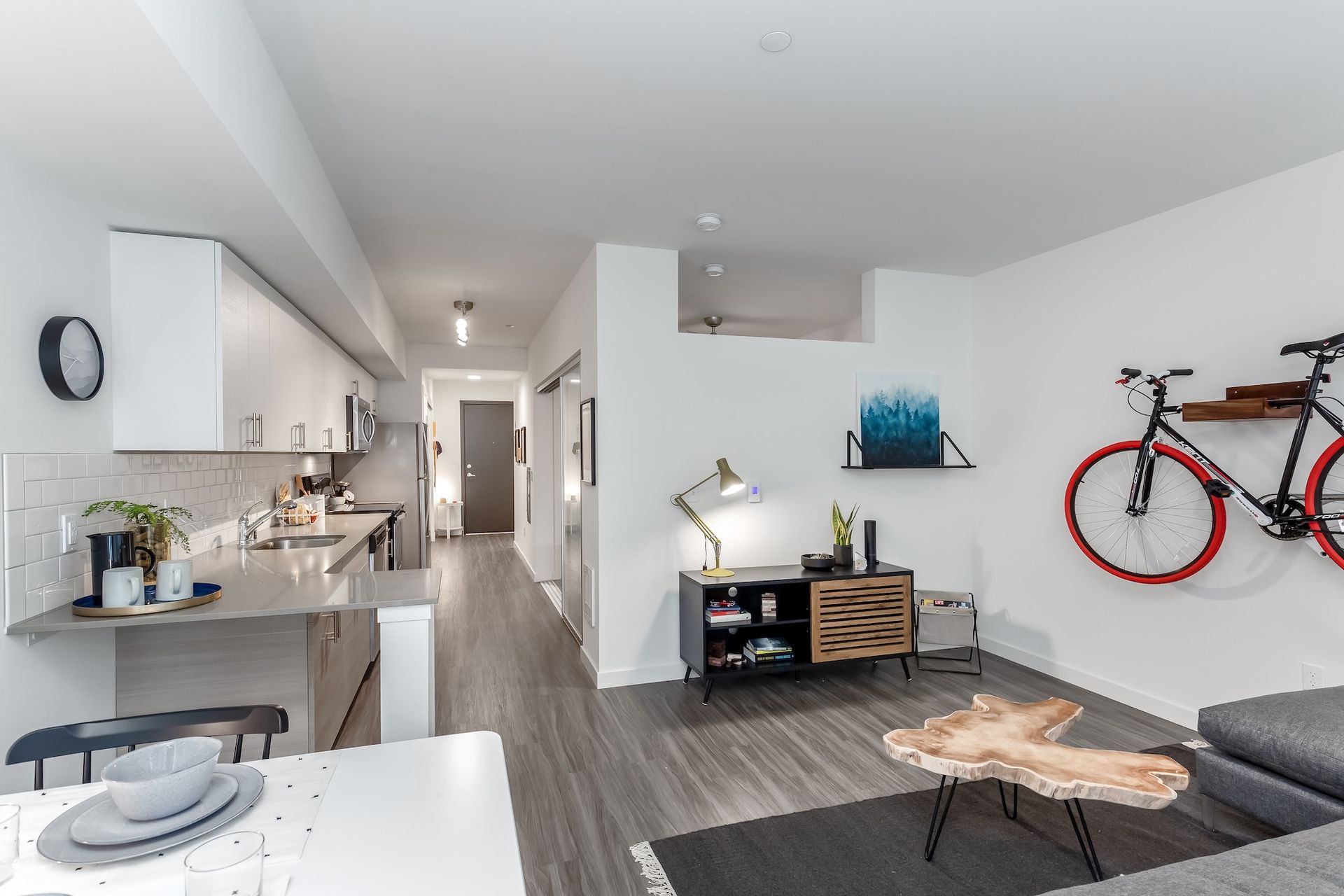 Modern, minimalist apartment interior. Kitchen, living area, and a bike mounted on the wall are visible.