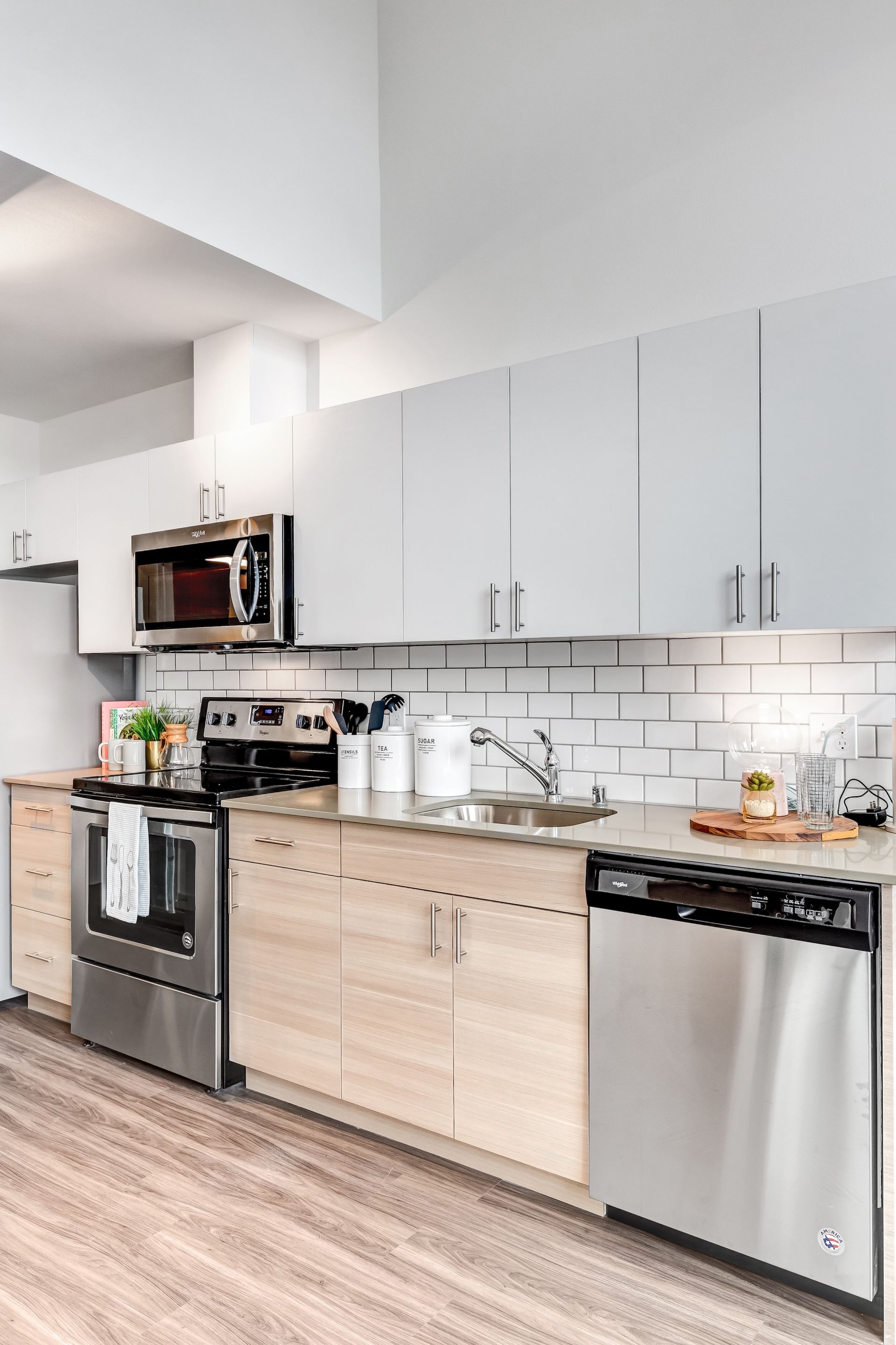 Modern kitchen with stainless steel appliances, light wood and grey cabinets, and white subway tile backsplash.