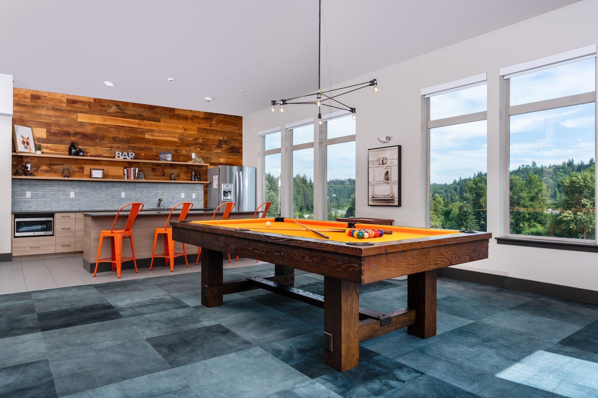 Game room with pool table, kitchen, large windows overlooking a forest, and orange chairs.