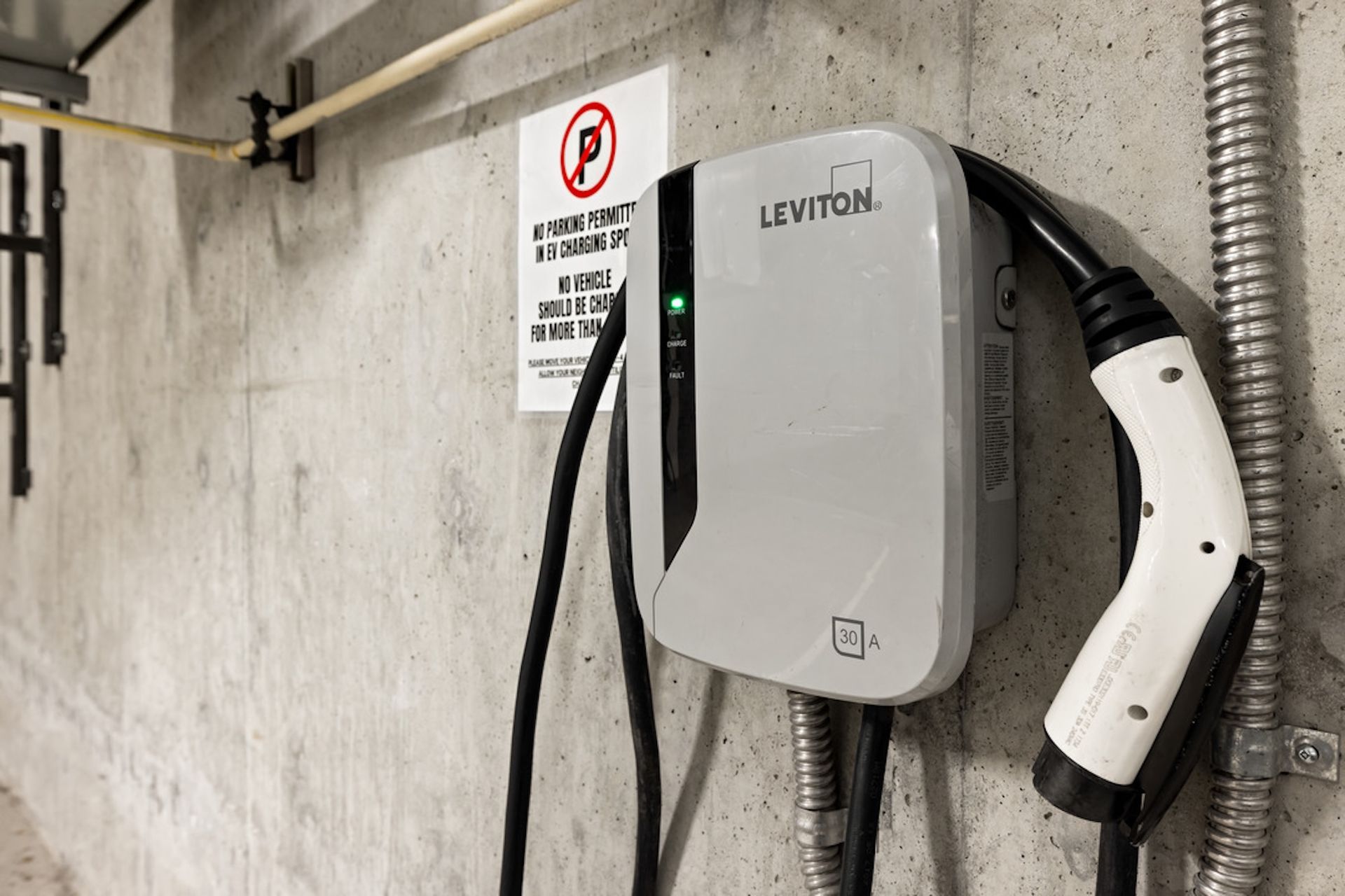 Leviton electric vehicle charger on concrete wall, charging cable plugged in.