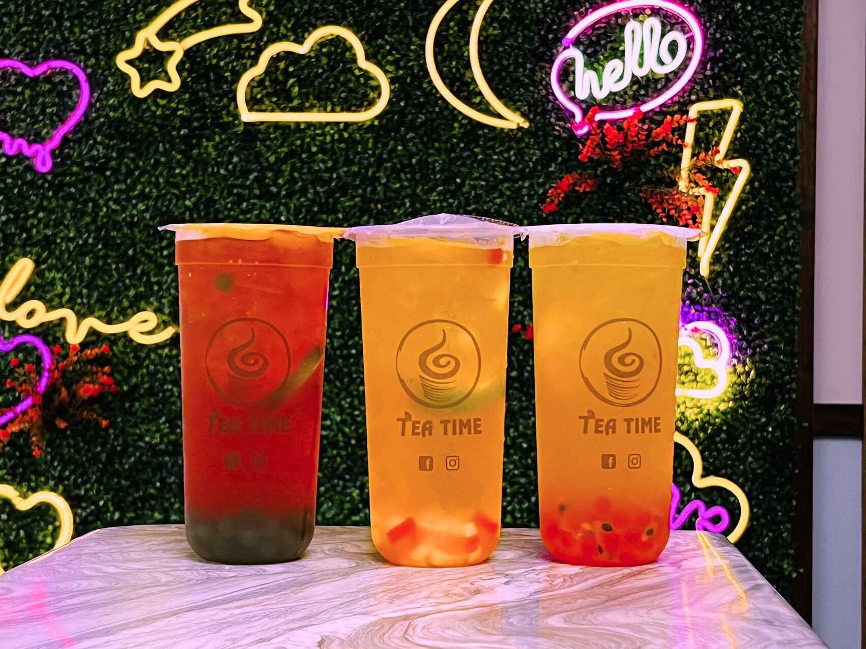 Three cups of tea are sitting on a table in front of a neon sign.