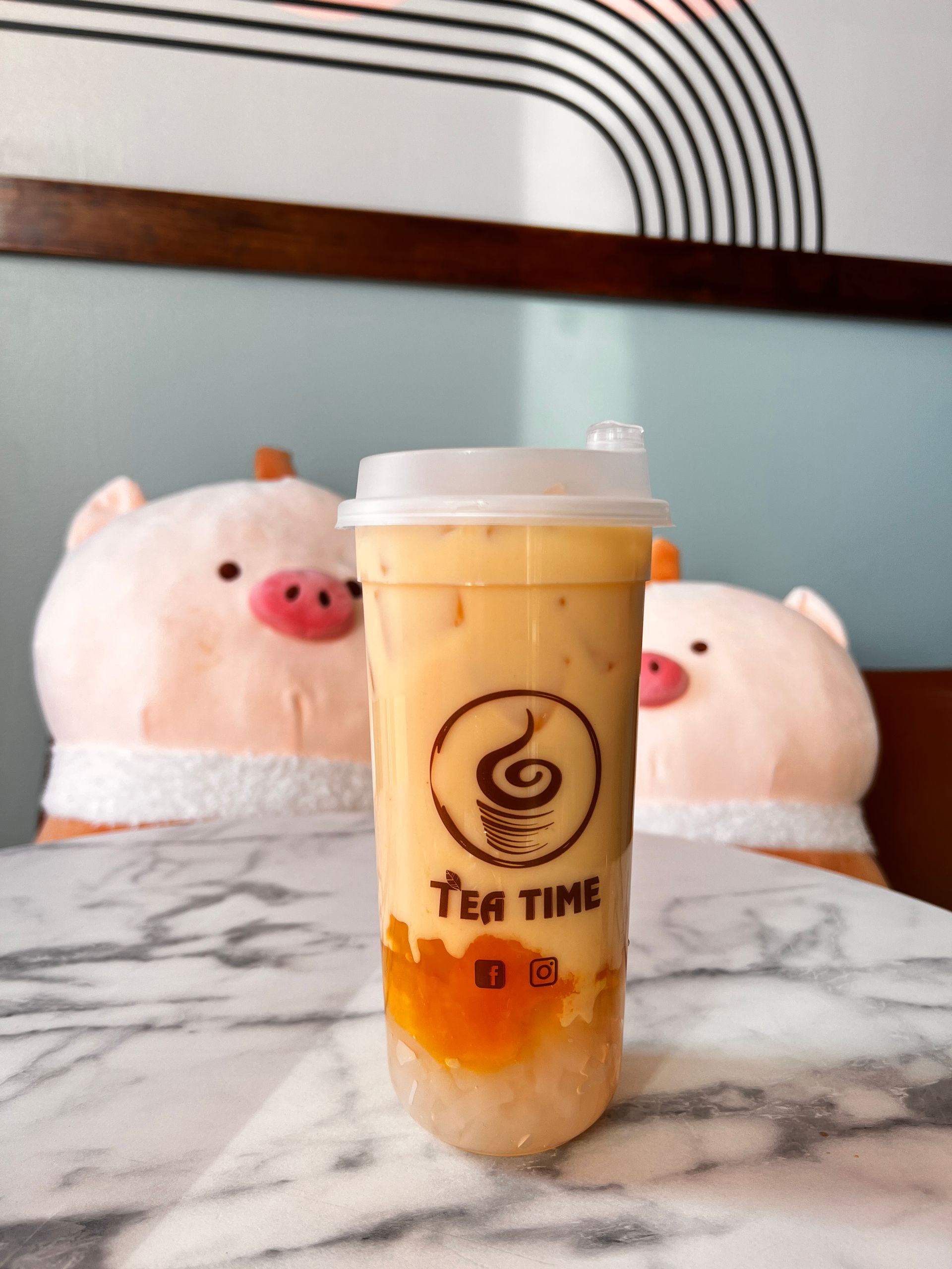A cup of tea time sits on a table in front of stuffed pigs
