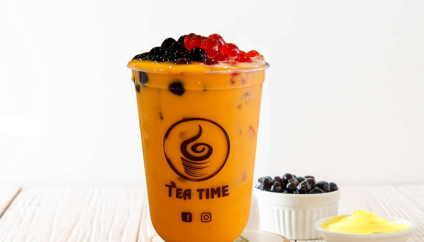 A cup of orange tea with bubbles on top is sitting on a wooden table.