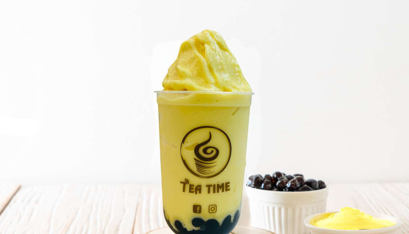 A green smoothie in a cup is sitting on a wooden table.