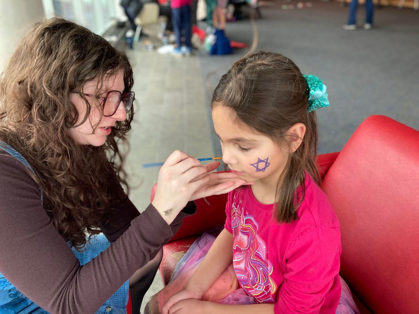 A woman is painting a little girl 's face with a brush.