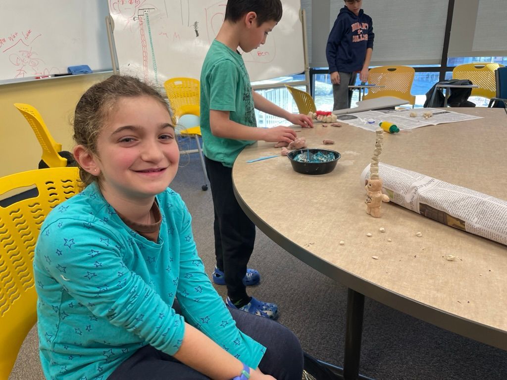 A girl is sitting at a table with a boy standing behind her.