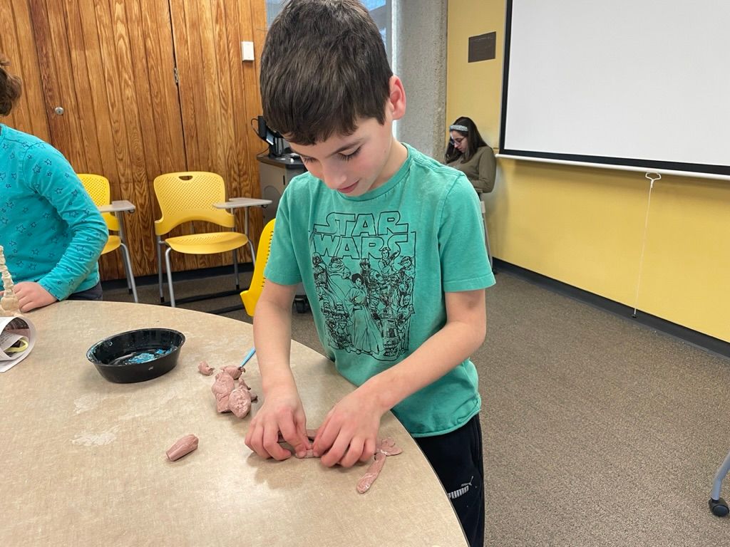 A young boy is sitting at a table playing with clay.