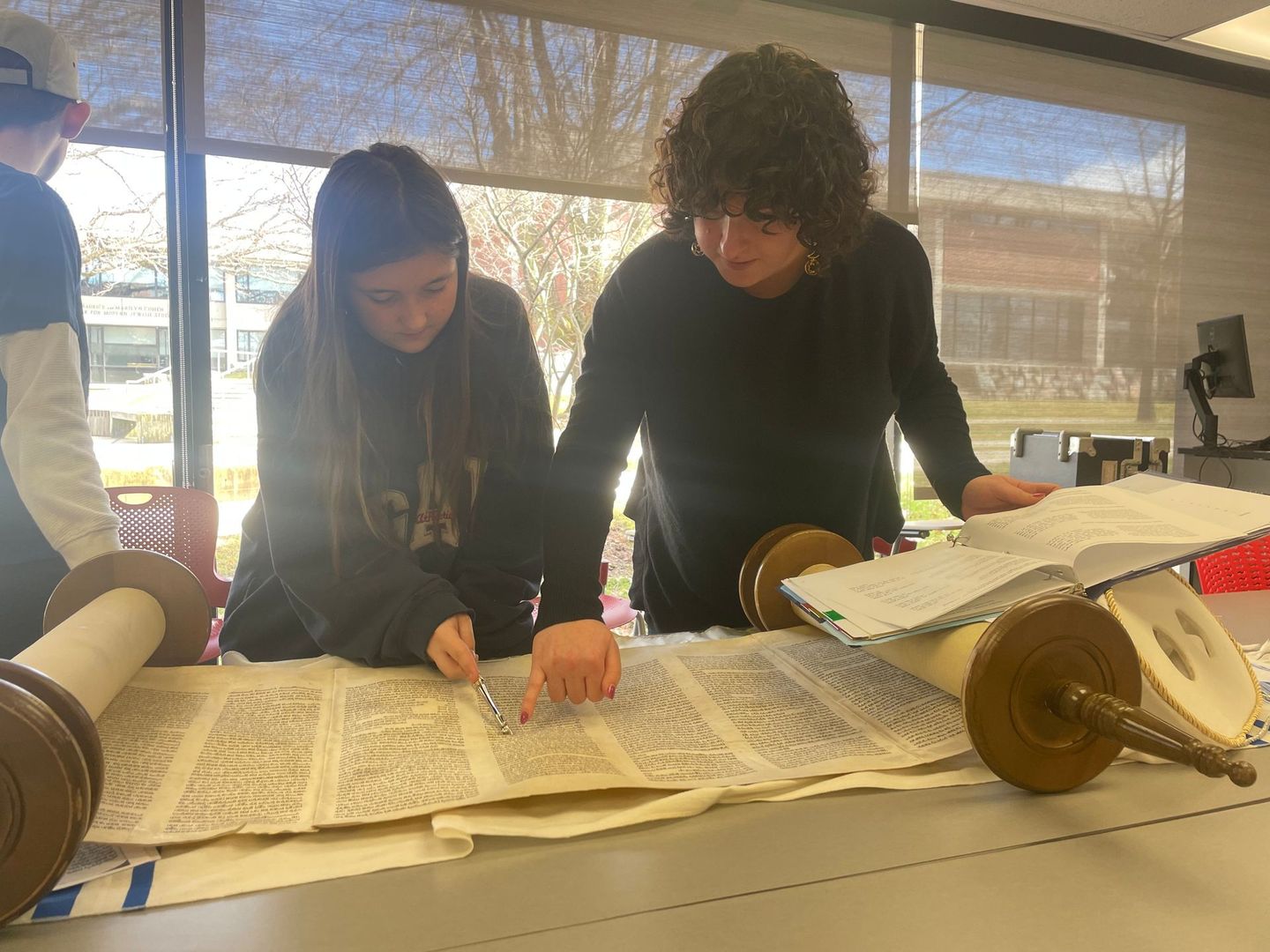 Two women are looking at a torah on a table.