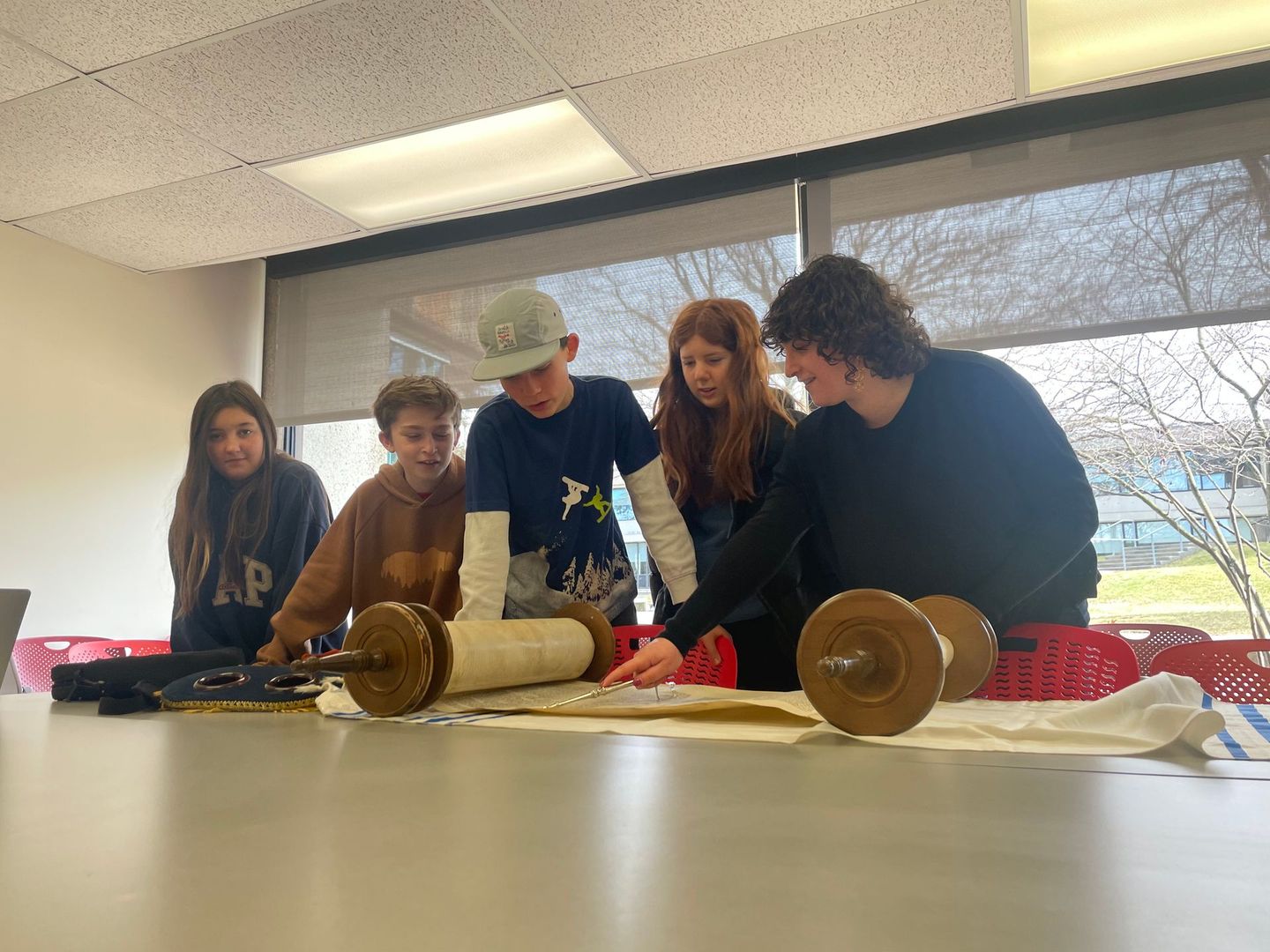 A group of young people are sitting around a table looking at a scroll.