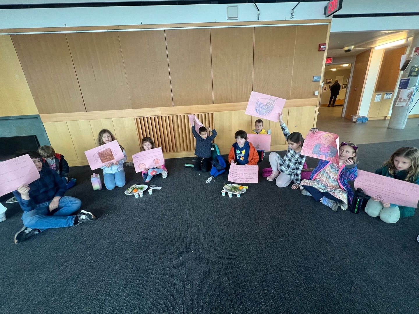 A group of children are sitting on the floor holding pink signs.