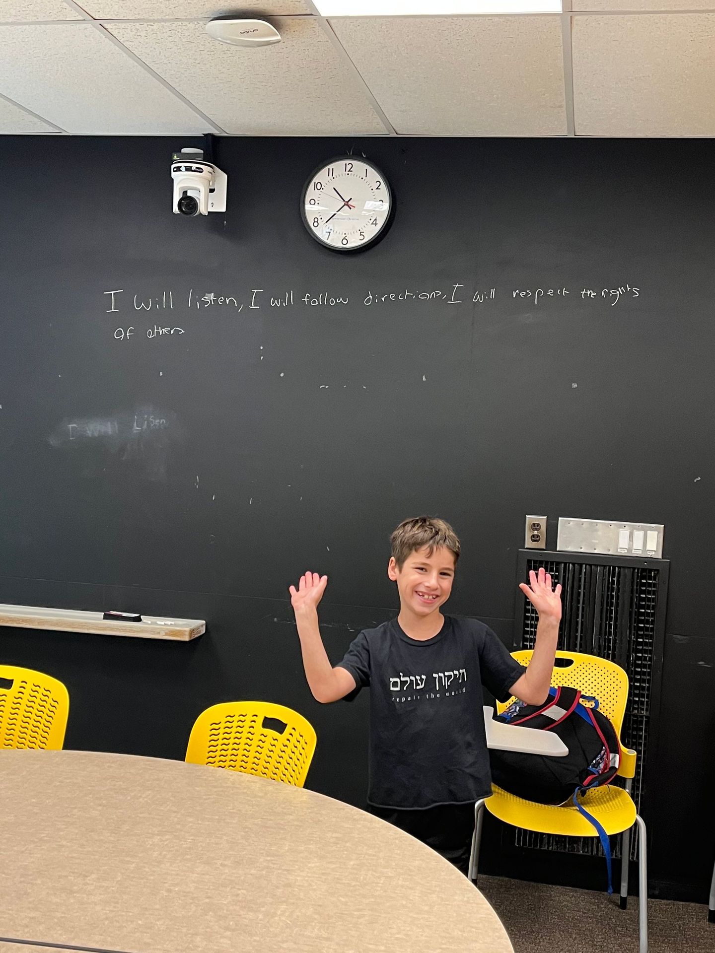 A boy is standing in front of a blackboard in a classroom