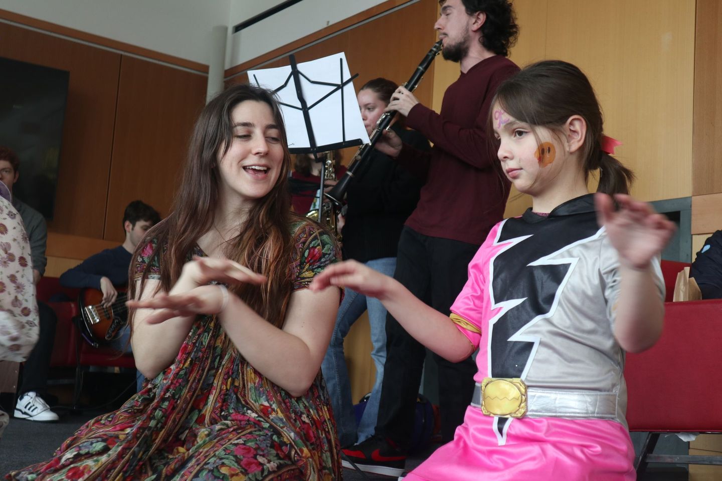 A girl in a superhero costume is sitting next to a girl in a floral dress.