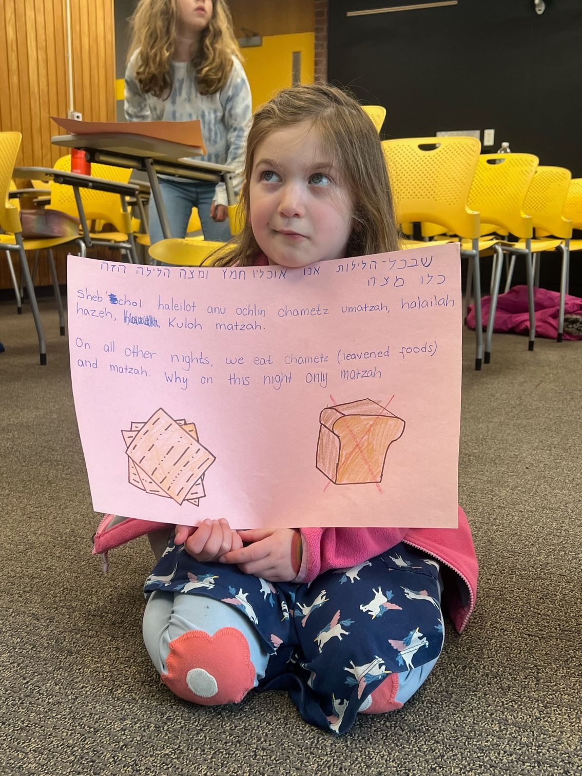 A little girl is sitting on the floor holding a piece of paper with a drawing on it.