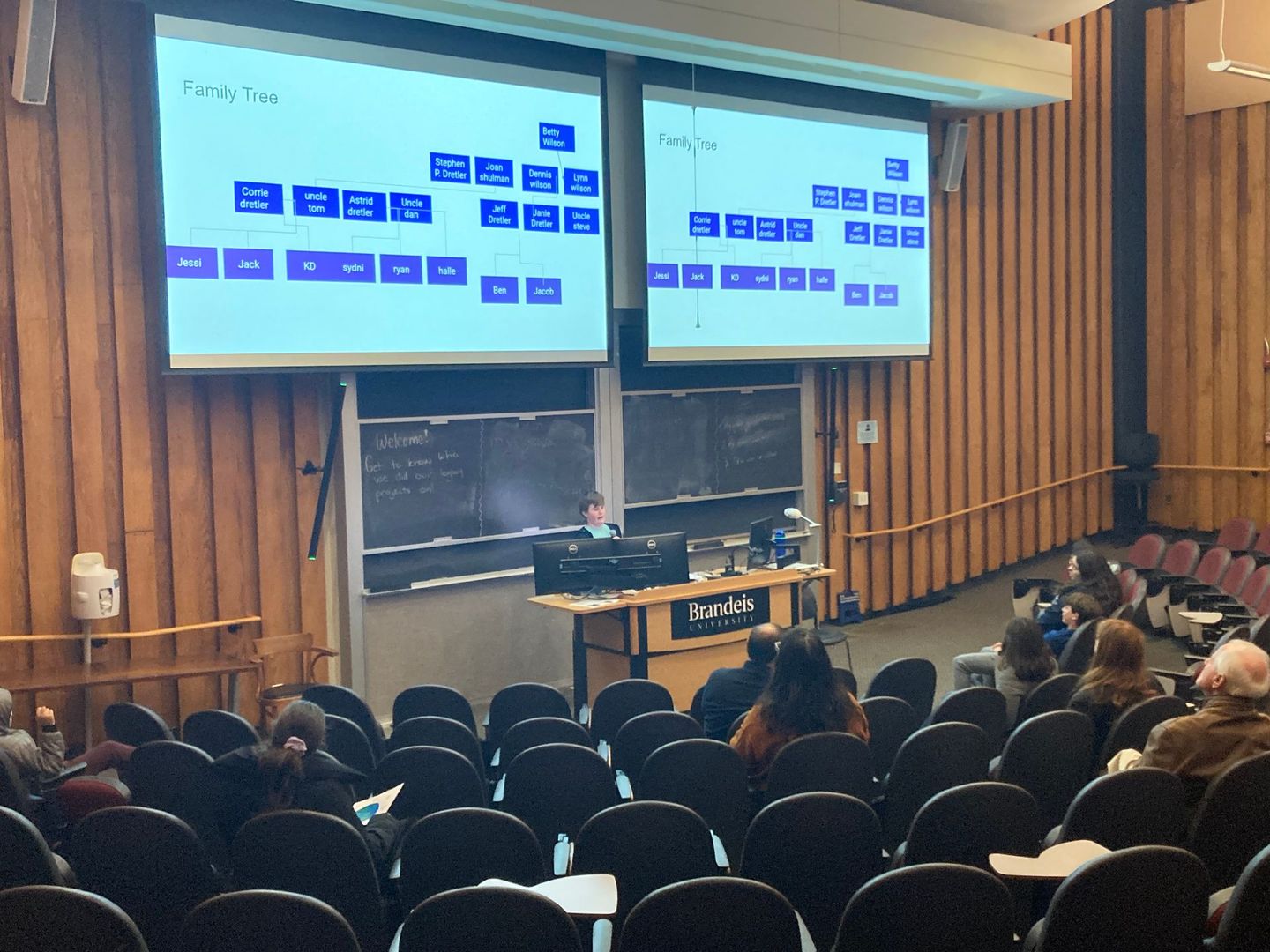 A group of people are sitting in a lecture hall watching a presentation