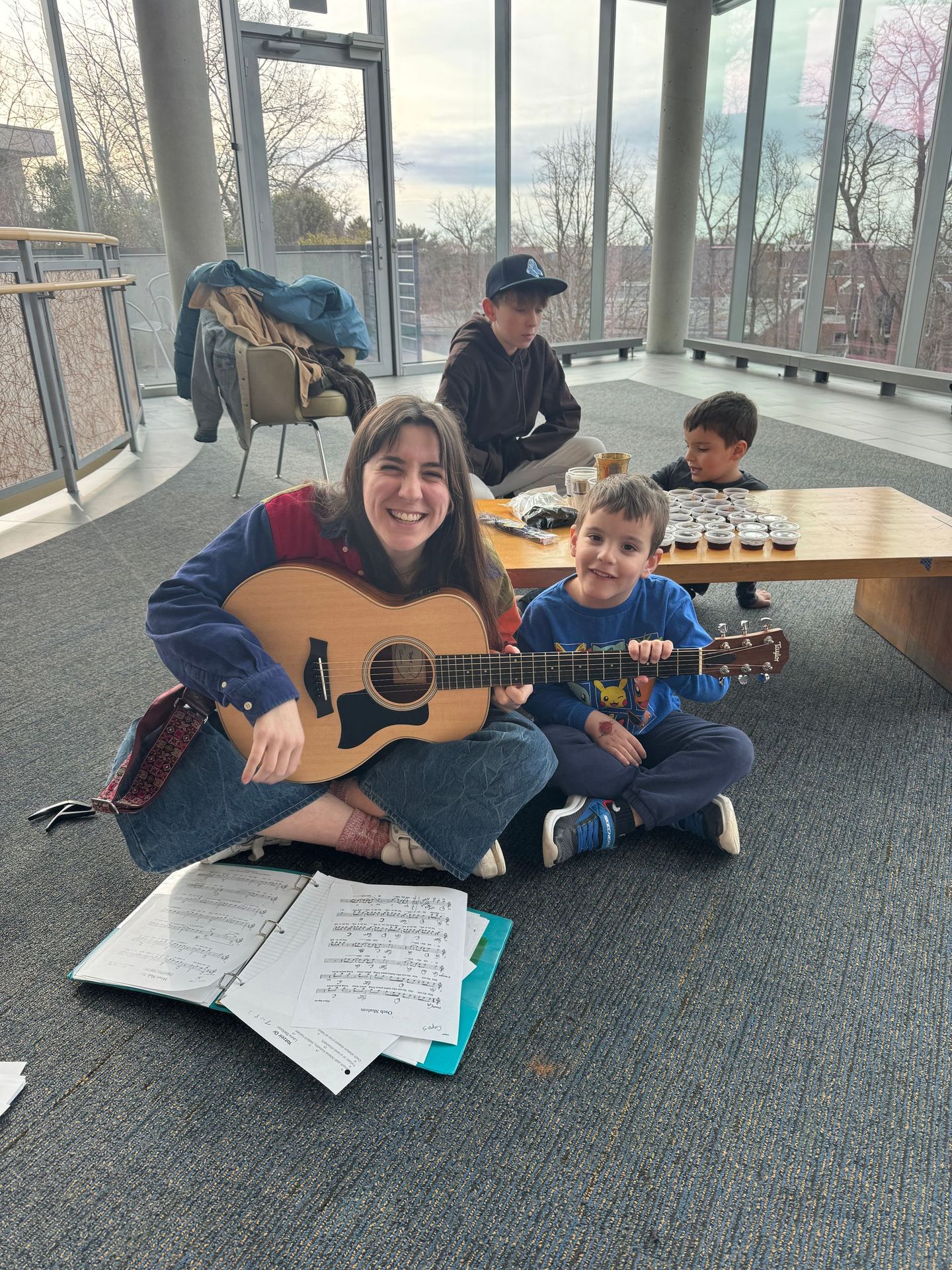 A woman is sitting on the floor playing a guitar with two children.