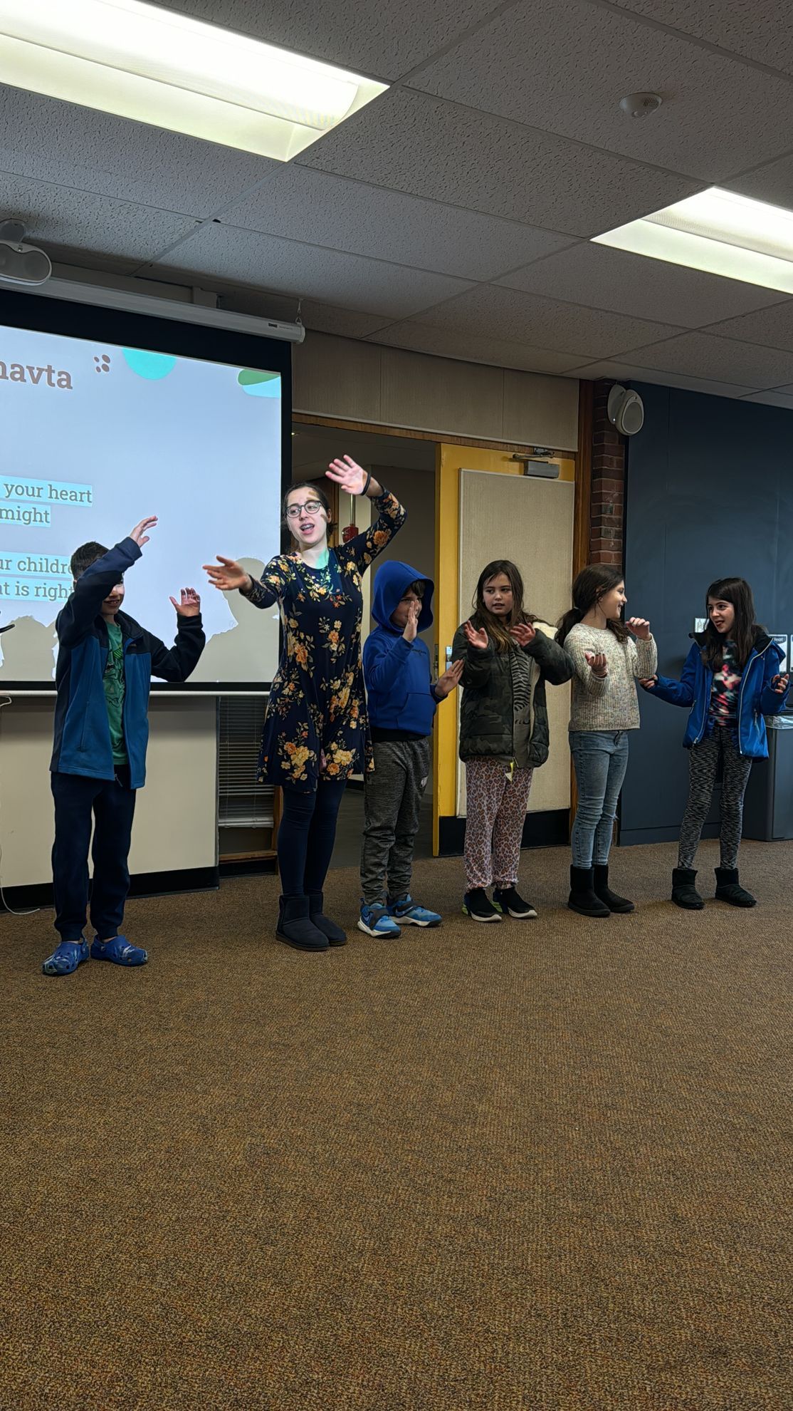 A group of children are standing on a stage in front of a projector screen.