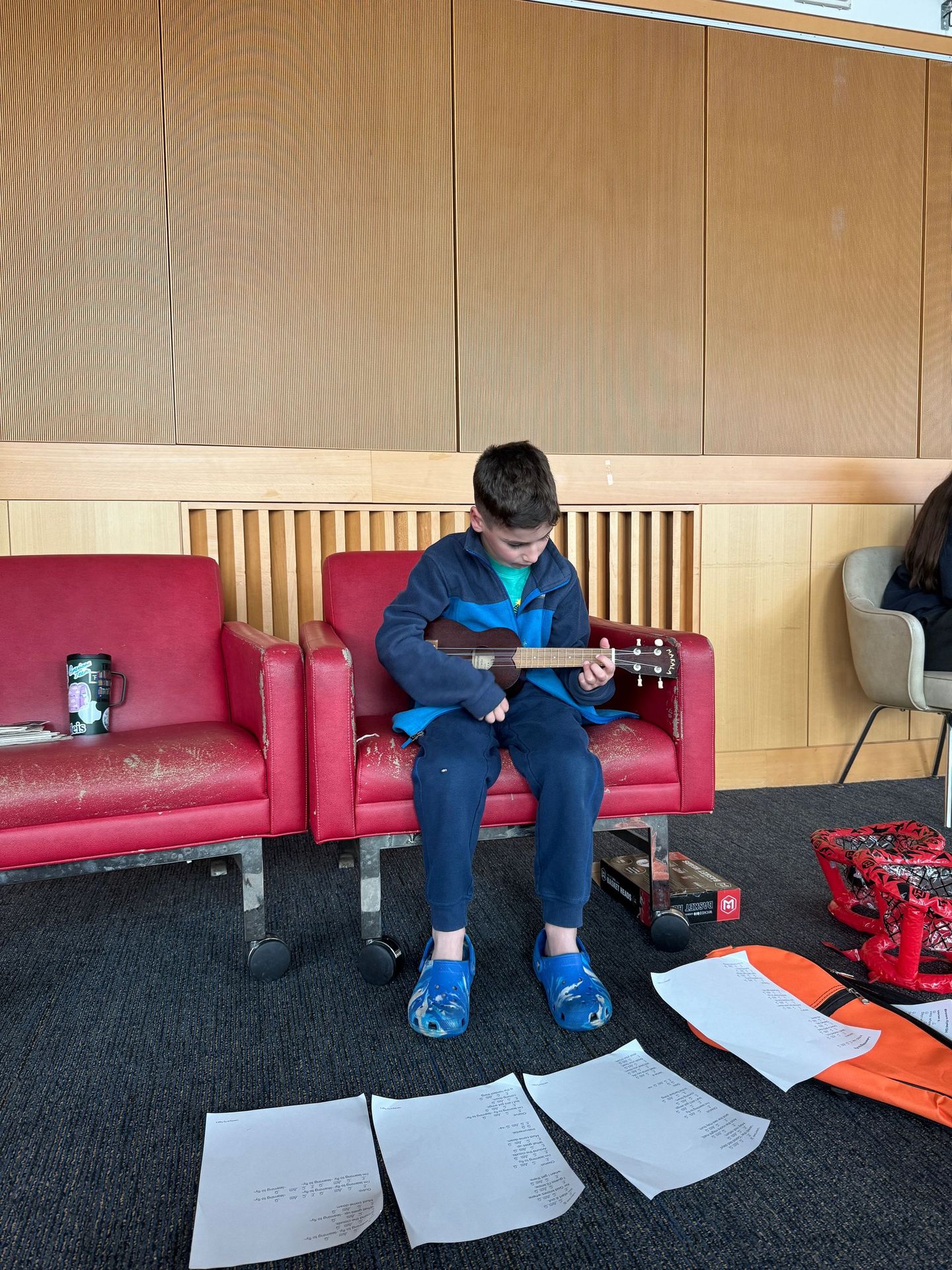 A young boy is sitting in a chair playing a guitar.