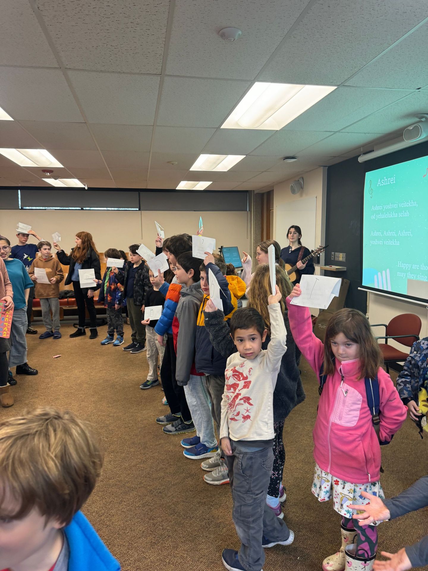 A group of children are standing in a room holding up papers.