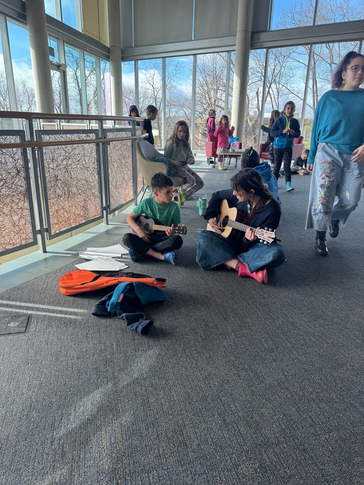 A group of children are sitting on the floor playing guitars.