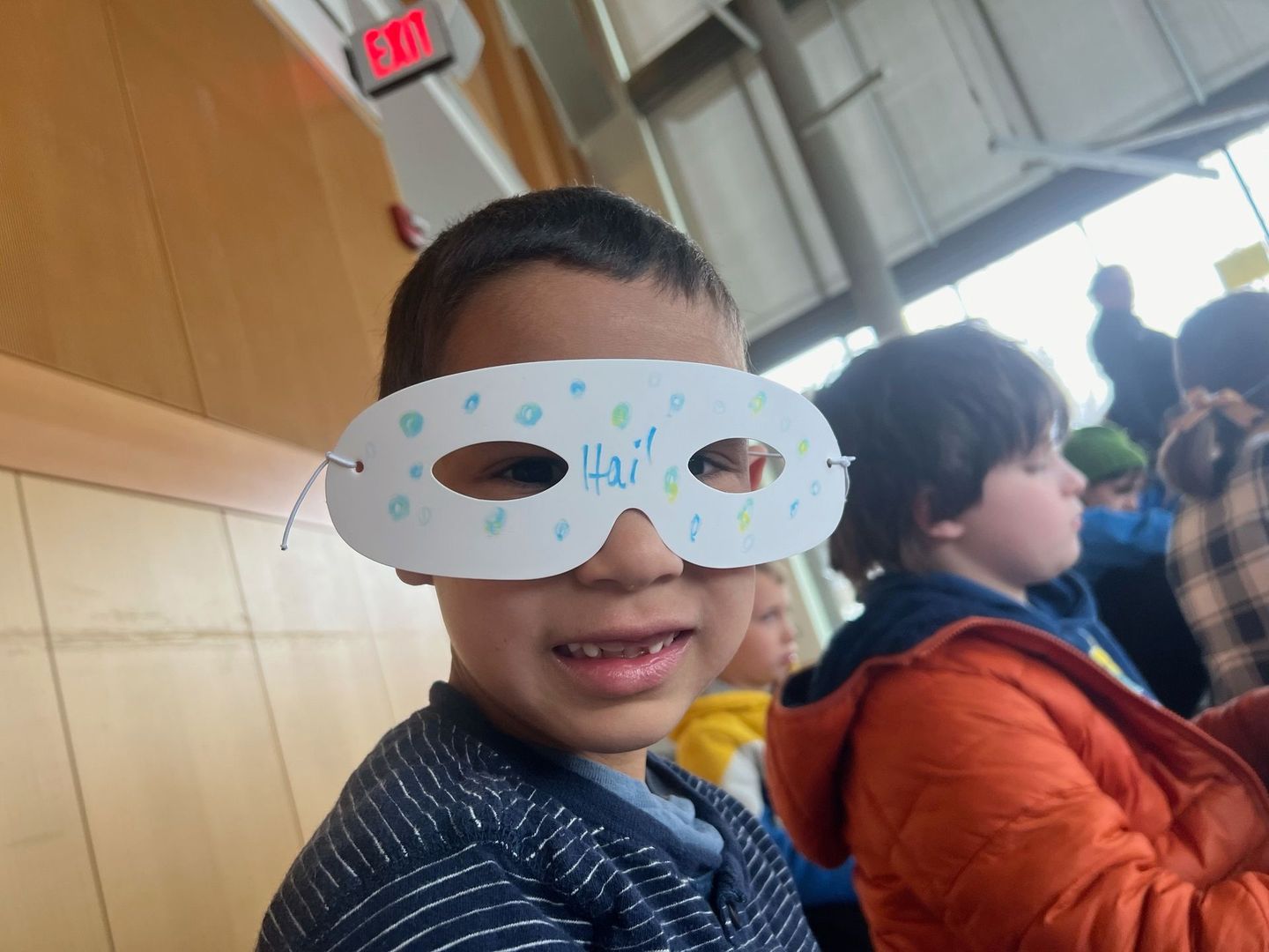 A young boy wearing a paper mask with the word hello written on it