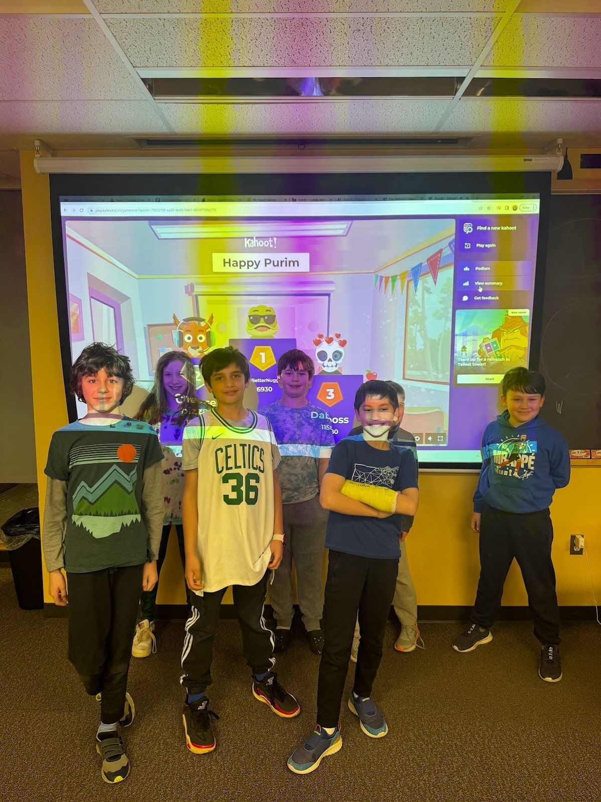 A group of children are standing in front of a large screen in a classroom.