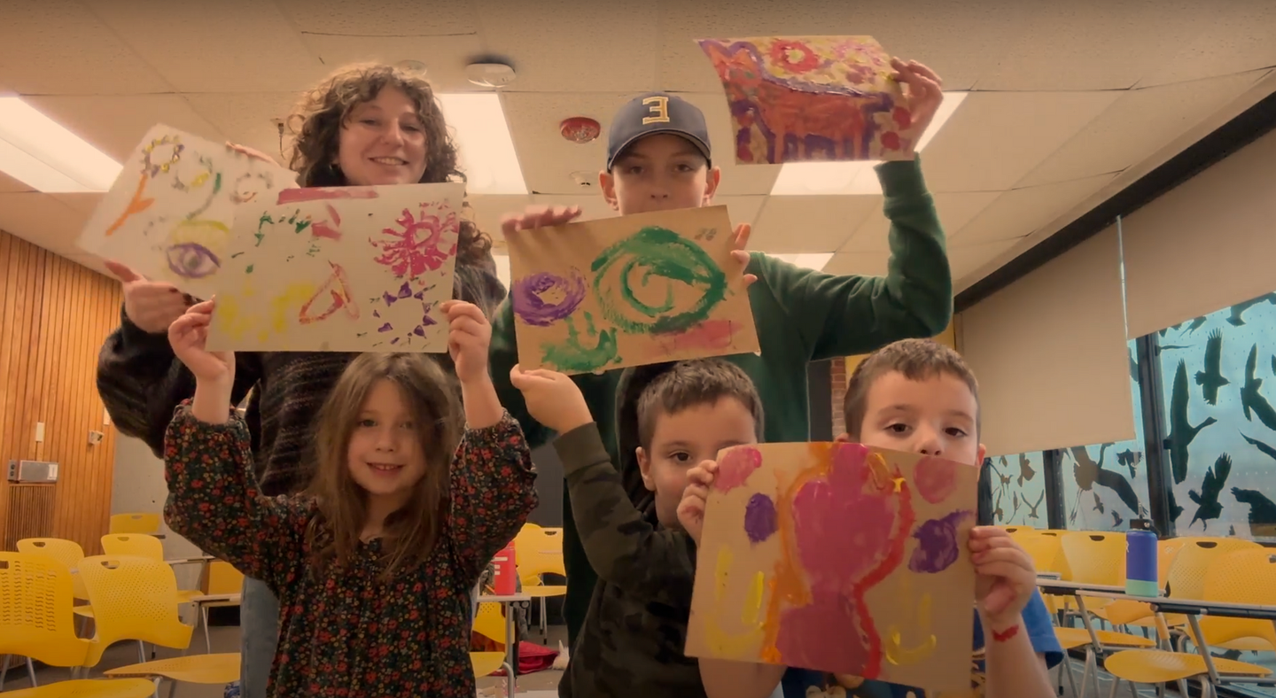 A group of children are holding up their paintings in a classroom.