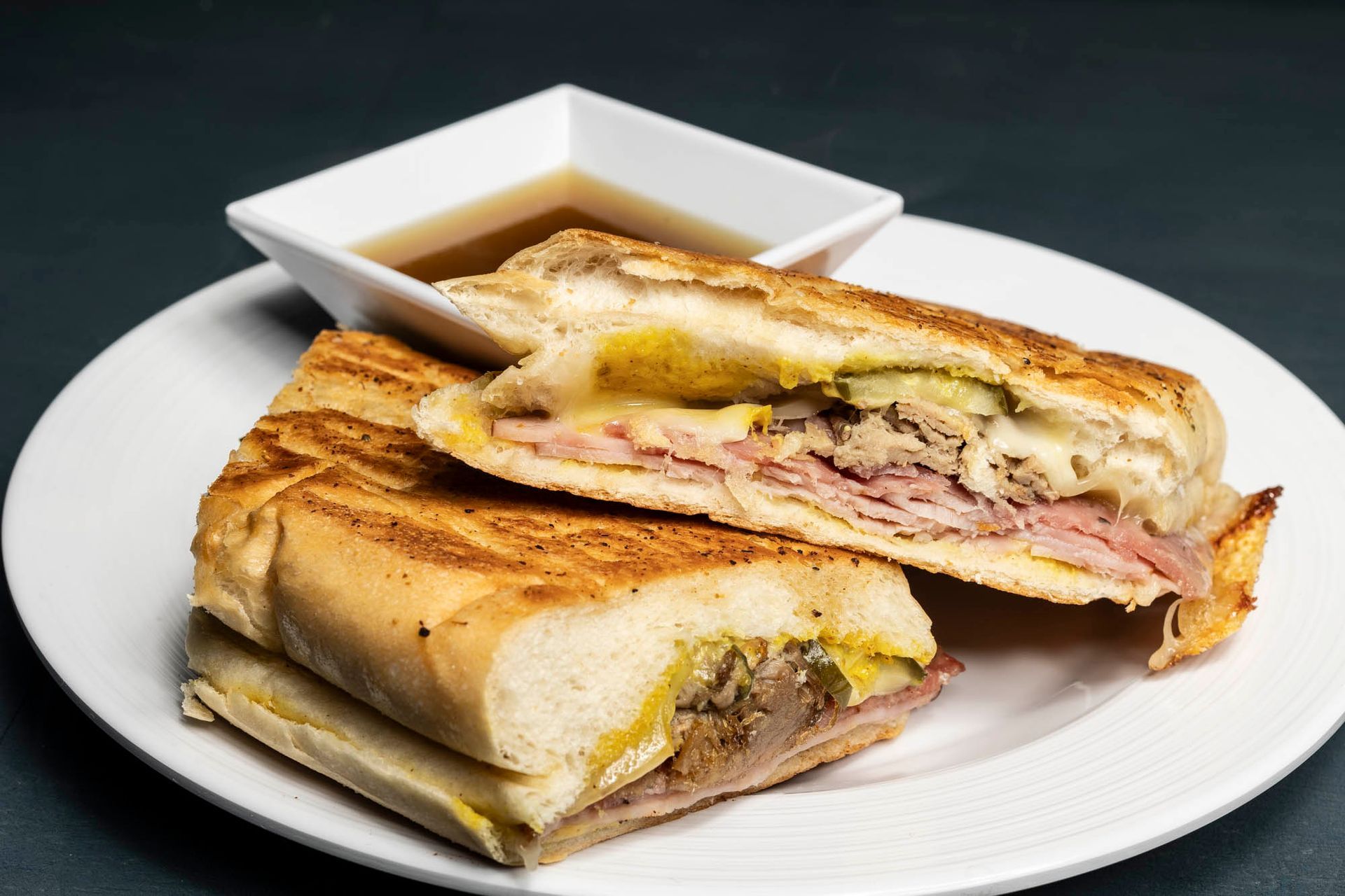 A Cuban sandwich on a white plate with a Mojo dipping sauce.