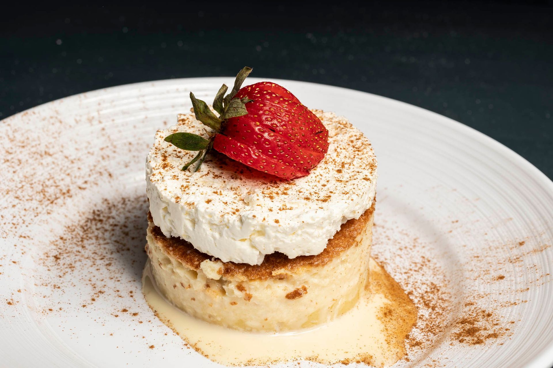 A white plate topped with a Tres Leches dessert with whipped cream and a strawberry on top.