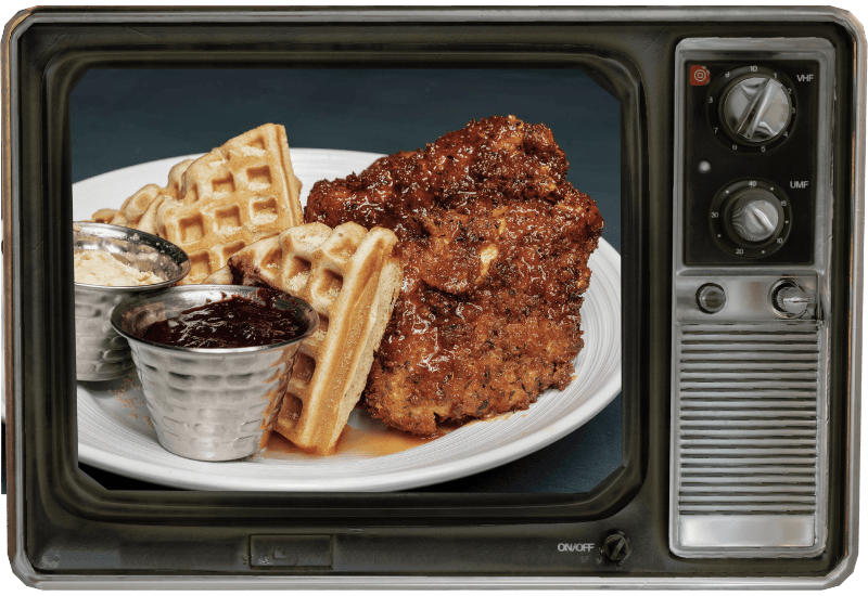 A tv screen shows a plate of food with waffles and chicken