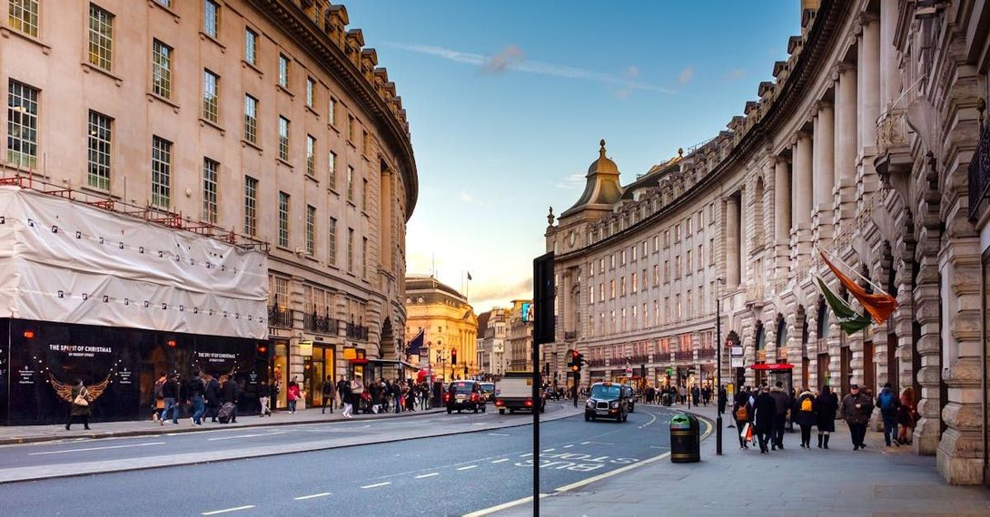A view of Regent Street in London, showing its iconic curved architecture, storefronts, and pedestrians on the sidewalk.
