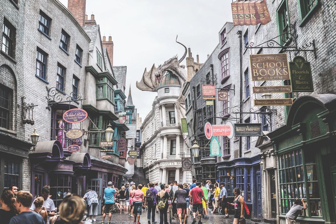 Crowds walk down Diagon Alley in Universal Studios, with a large dragon perched atop the Gringotts Bank building.