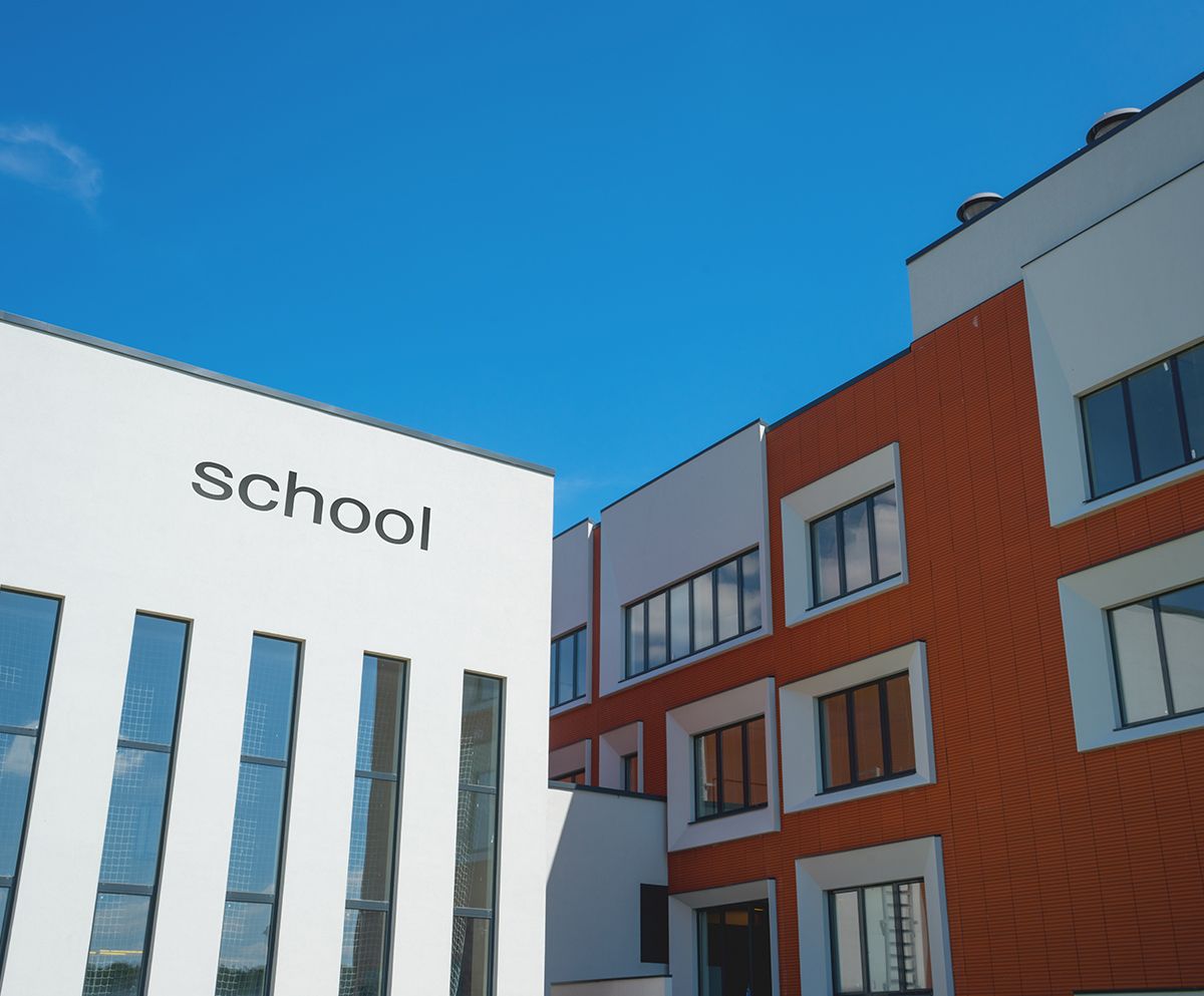 School buildings against a bright blue sky; one white with vertical windows, the other orange.