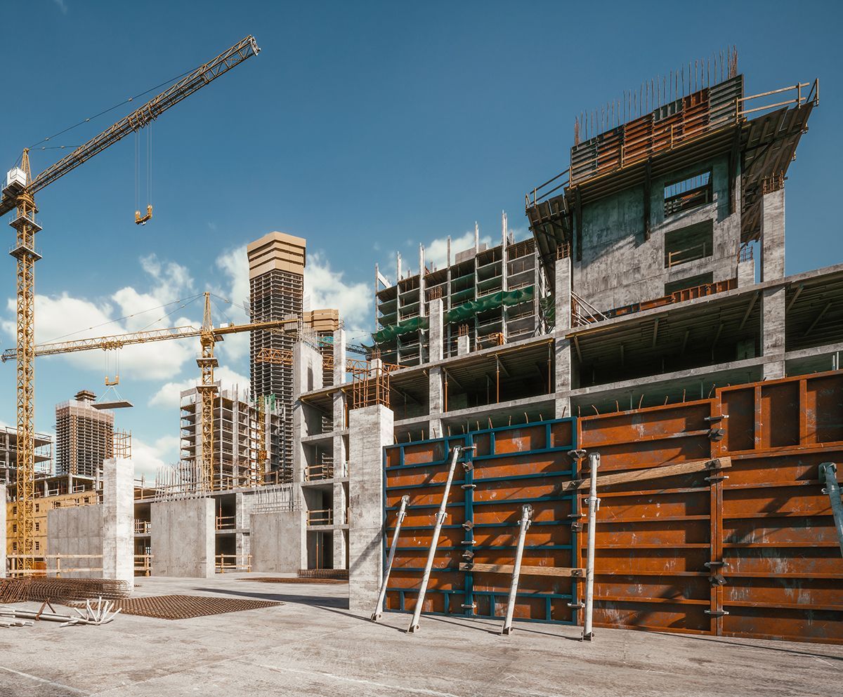 Construction site with multiple buildings under construction, cranes, blue sky.