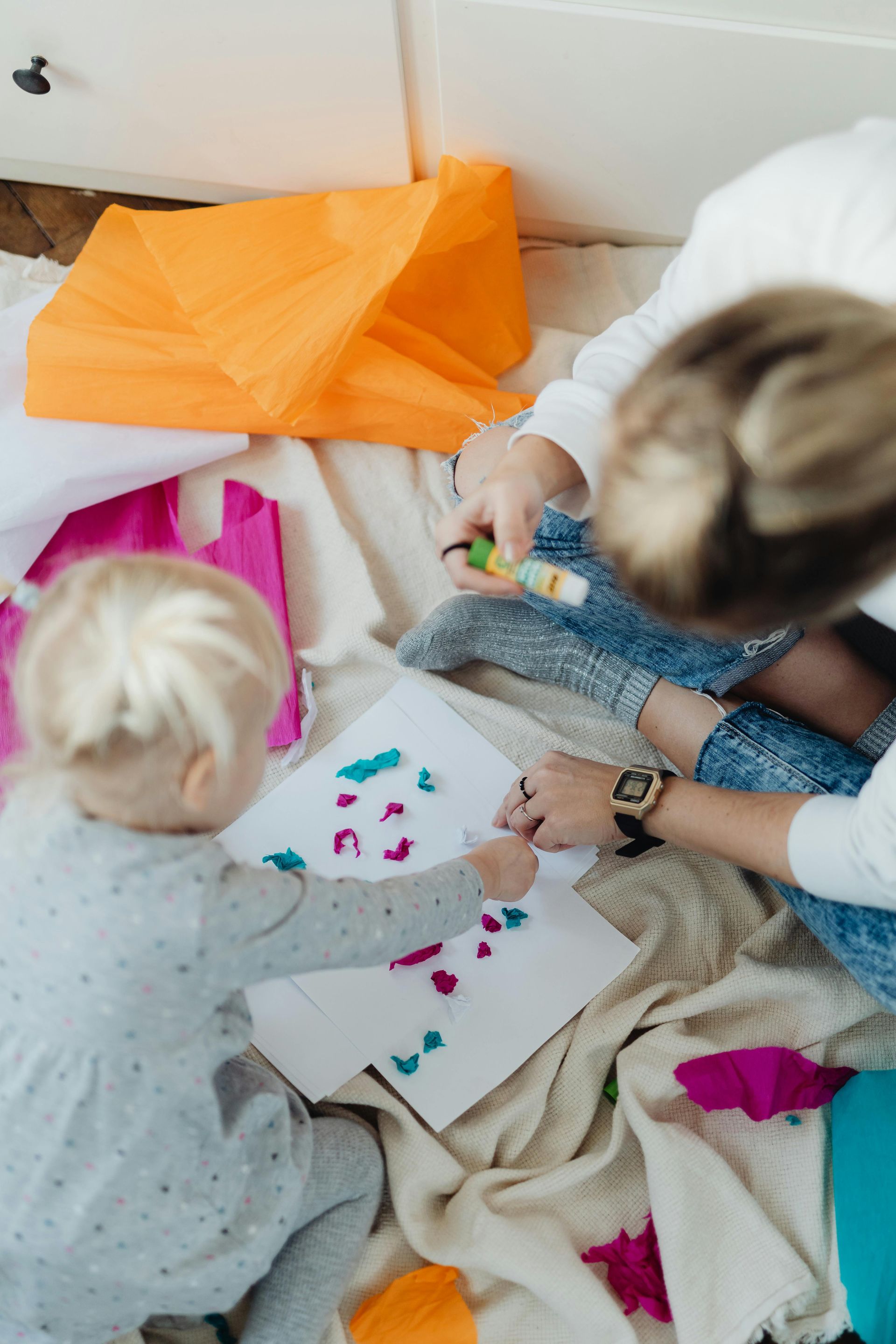 Woman assists a child coloring at a table in a classroom.
