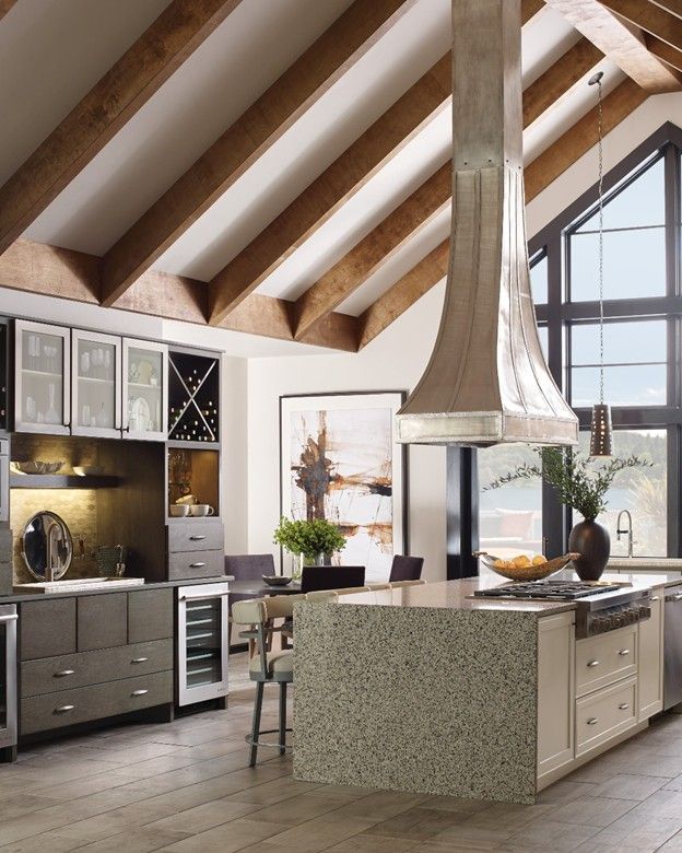 Rustic kitchen with island & cabinets. A large range hood hangs above the island with a picture window at the end.