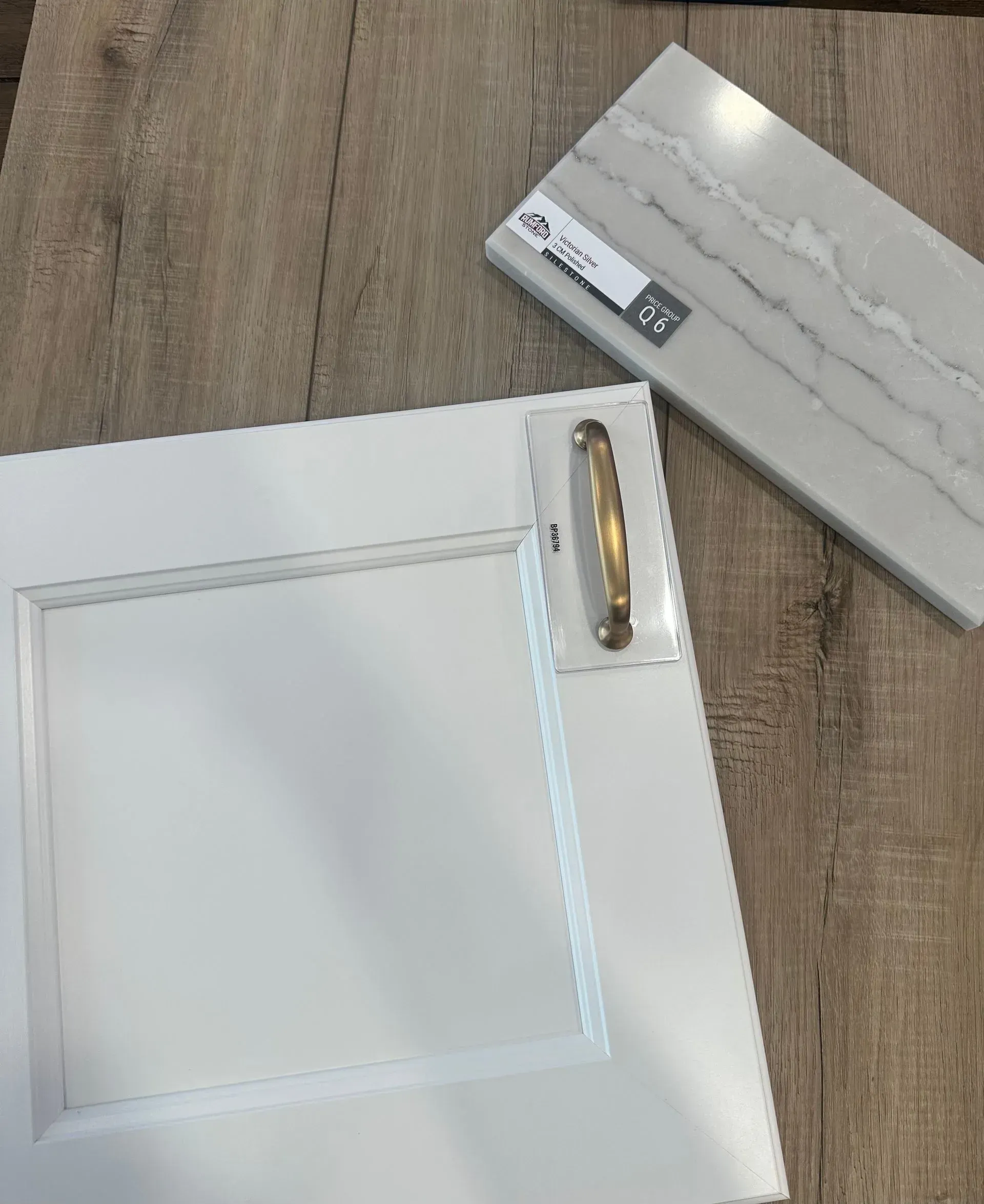 White cabinet door with gold handle, quartz countertop sample on wood background.