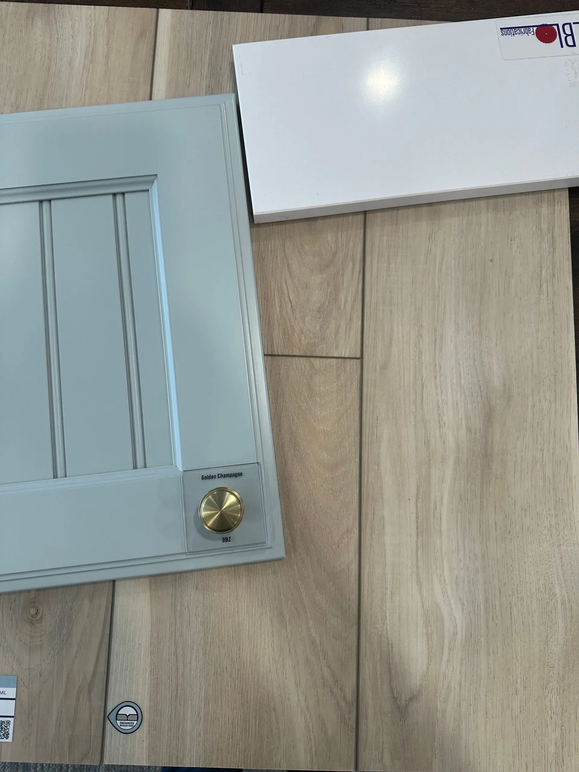 A light blue cabinet door with a gold knob and a white countertop sample on light-toned wood flooring.