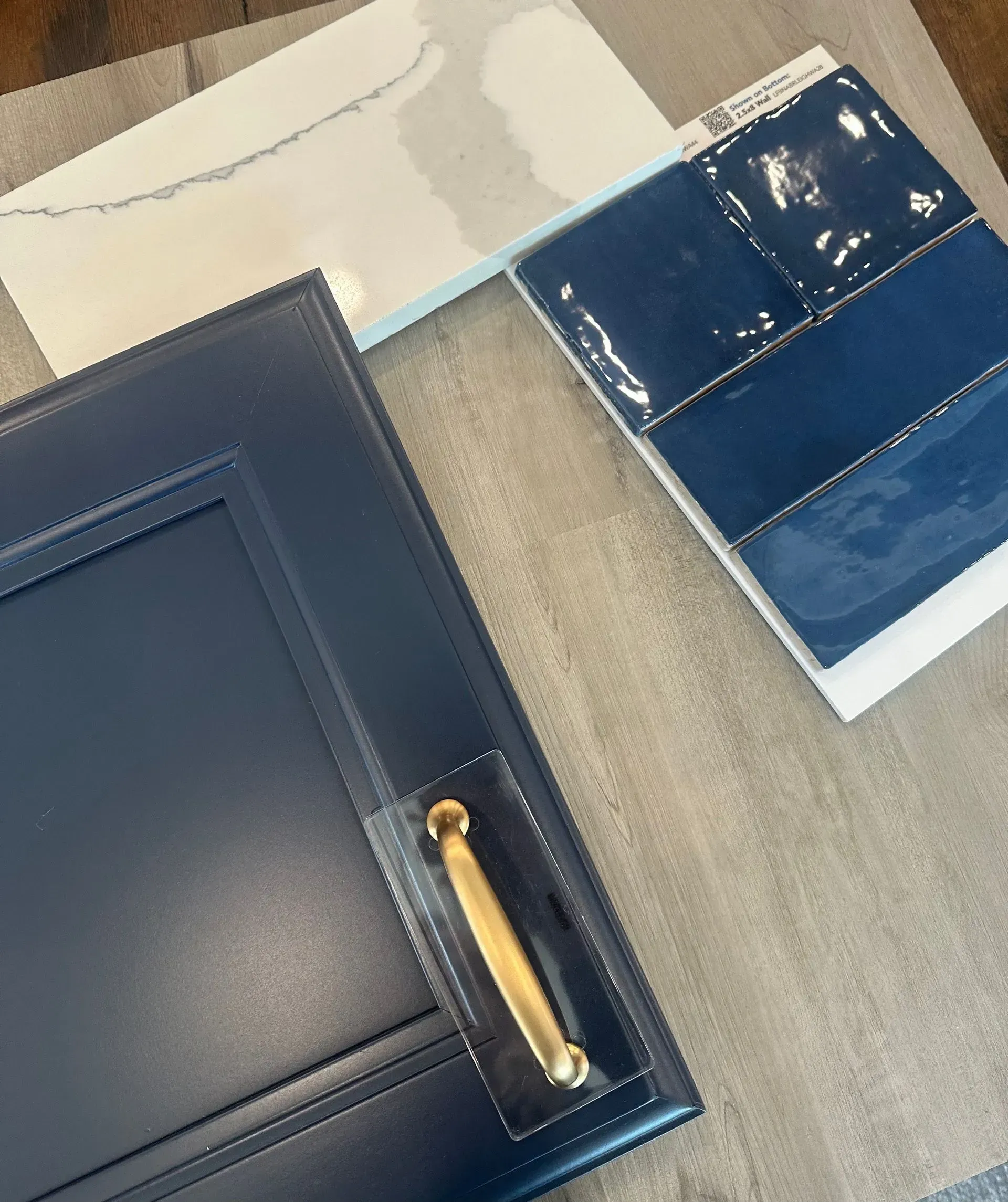 Navy blue cabinet door with gold handle, color swatches, and white paint samples on a light gray surface.