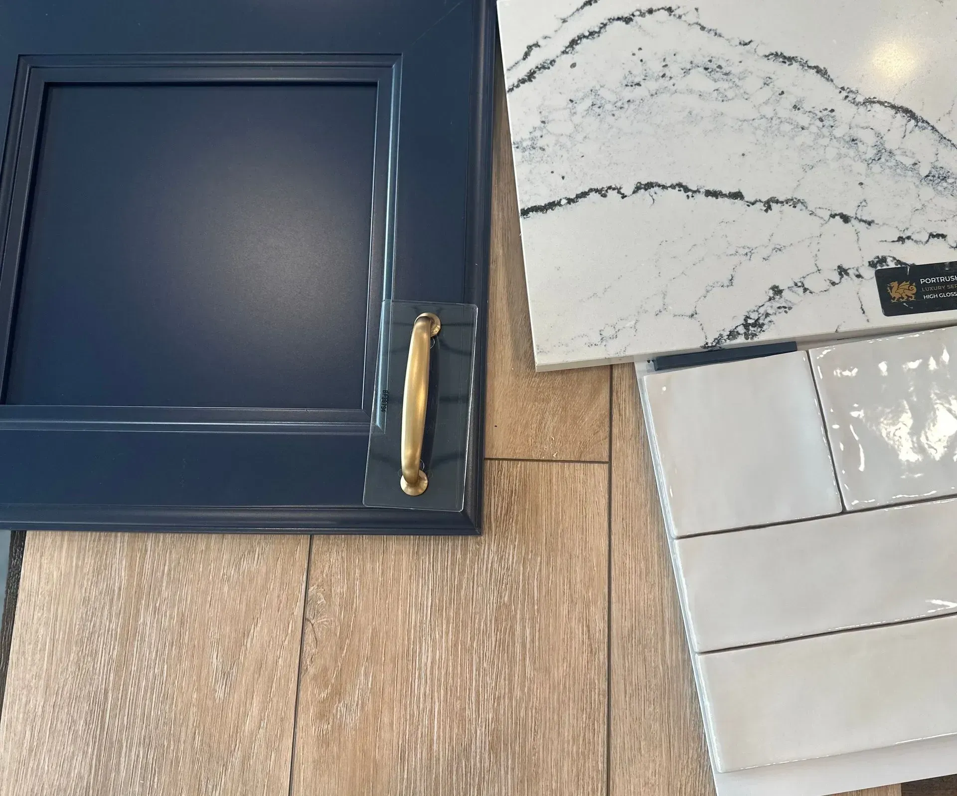 Navy blue cabinet door with gold handle, white countertop, white subway tiles, on wood.